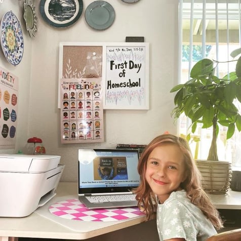 A female elementary student working at a laptop at a desk in her home